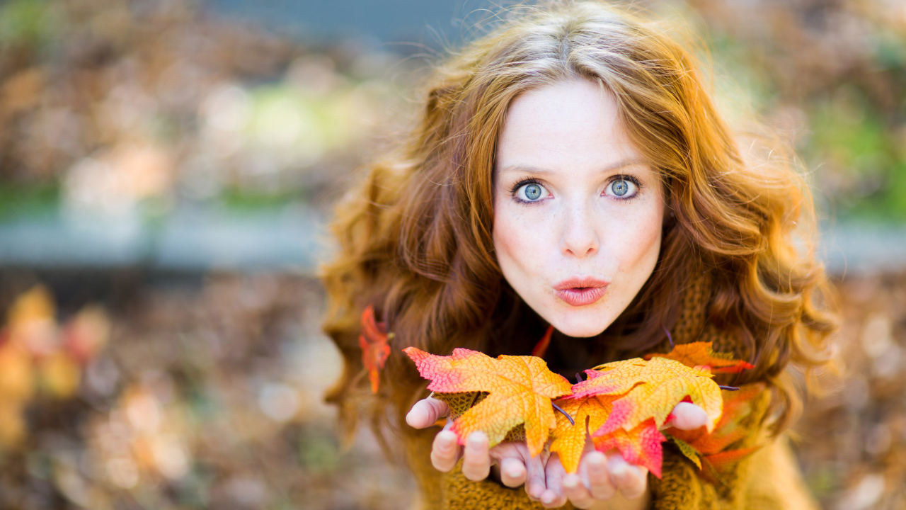 Красивая девушка сдувает листья с ладоней