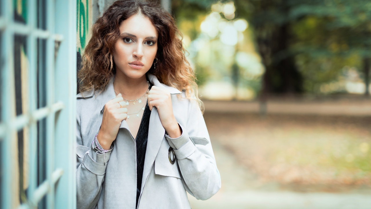 Красивая девушка в сером плаще у стены