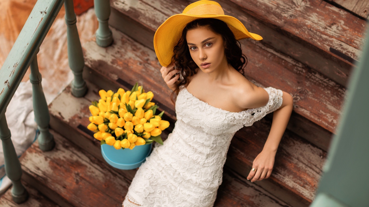 Красивая девушка в белом платье и желтой шляпе на ступеньках с букетом тюльпанов