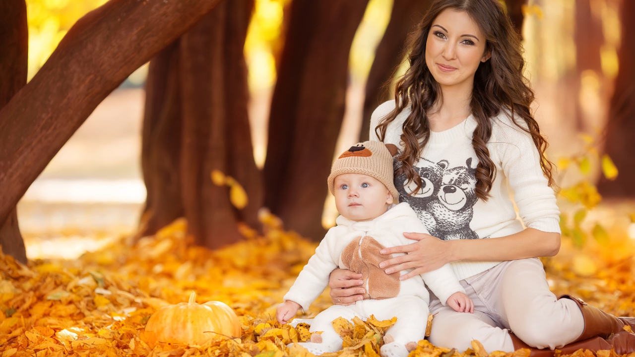 Красивая девушка сидит с грудным ребенком на опавшей листве