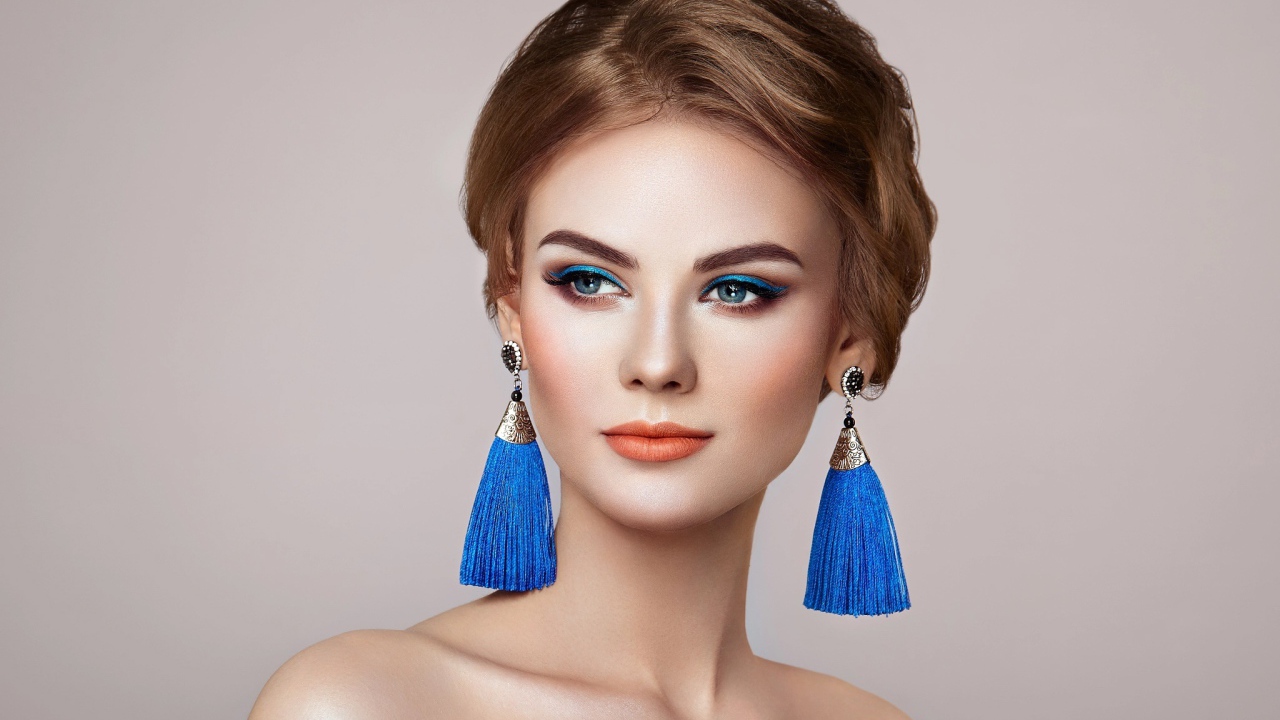 Красивая девушка с синими сережками на сером фоне
