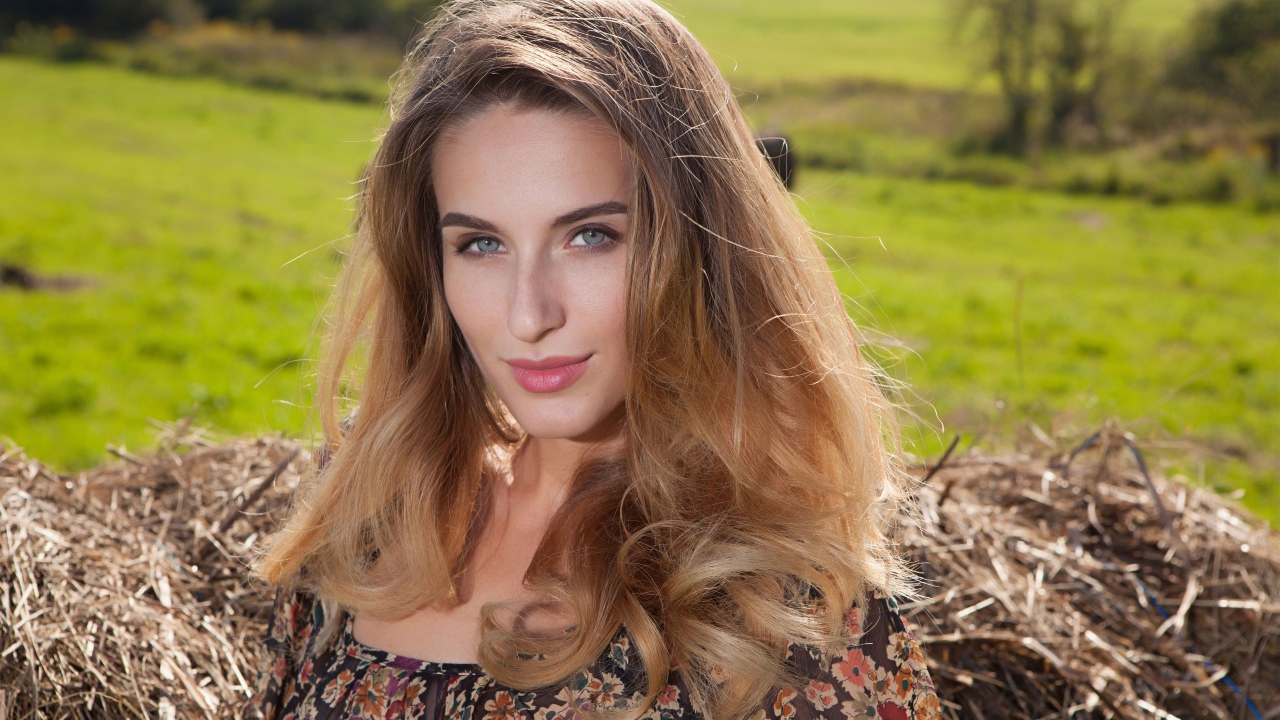 Красивая девушка с серыми глазами стоит у сена