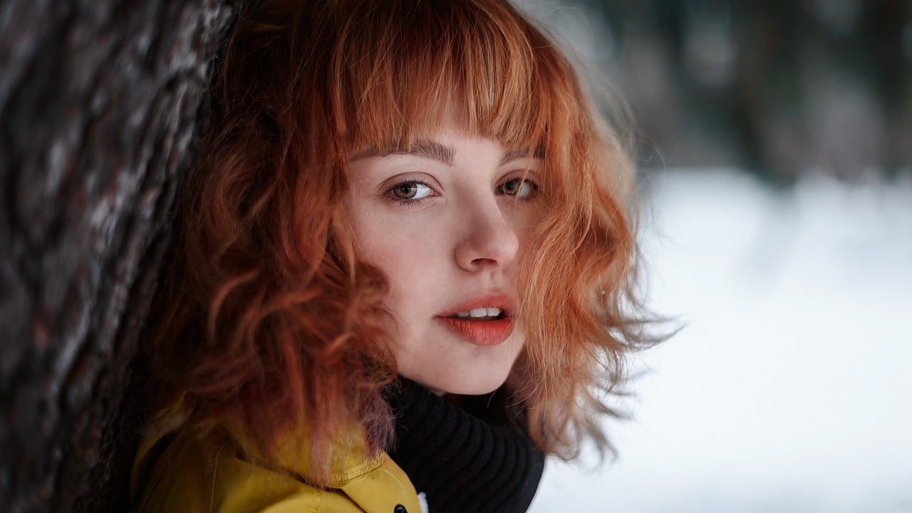 Красивая рыжеволосая девушка стоит у дерева зимой