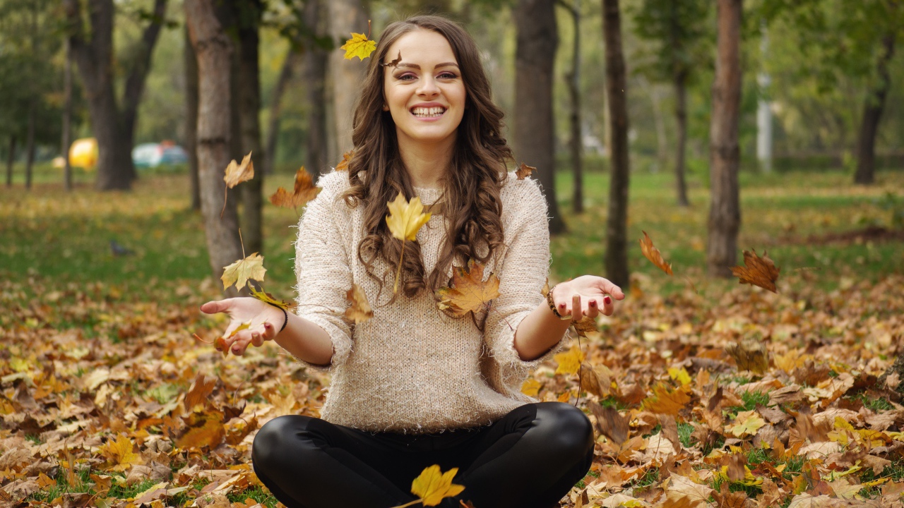 Красивая улыбающаяся девушка сидит на земле с желтыми листьями