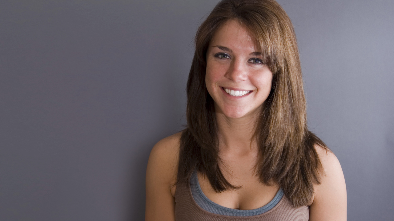 Улыбающаяся милая девушка у серой стены