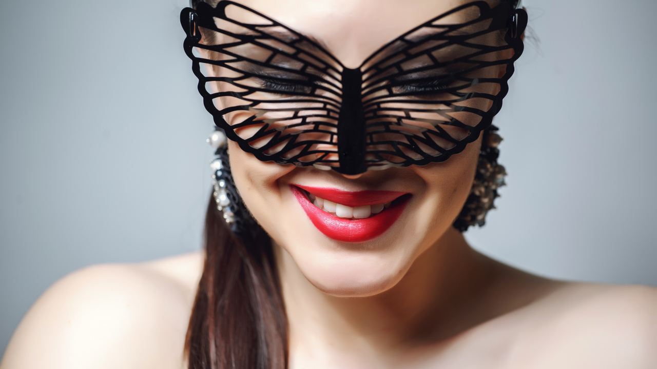 Улыбающаяся девушка в черной маске на сером фоне