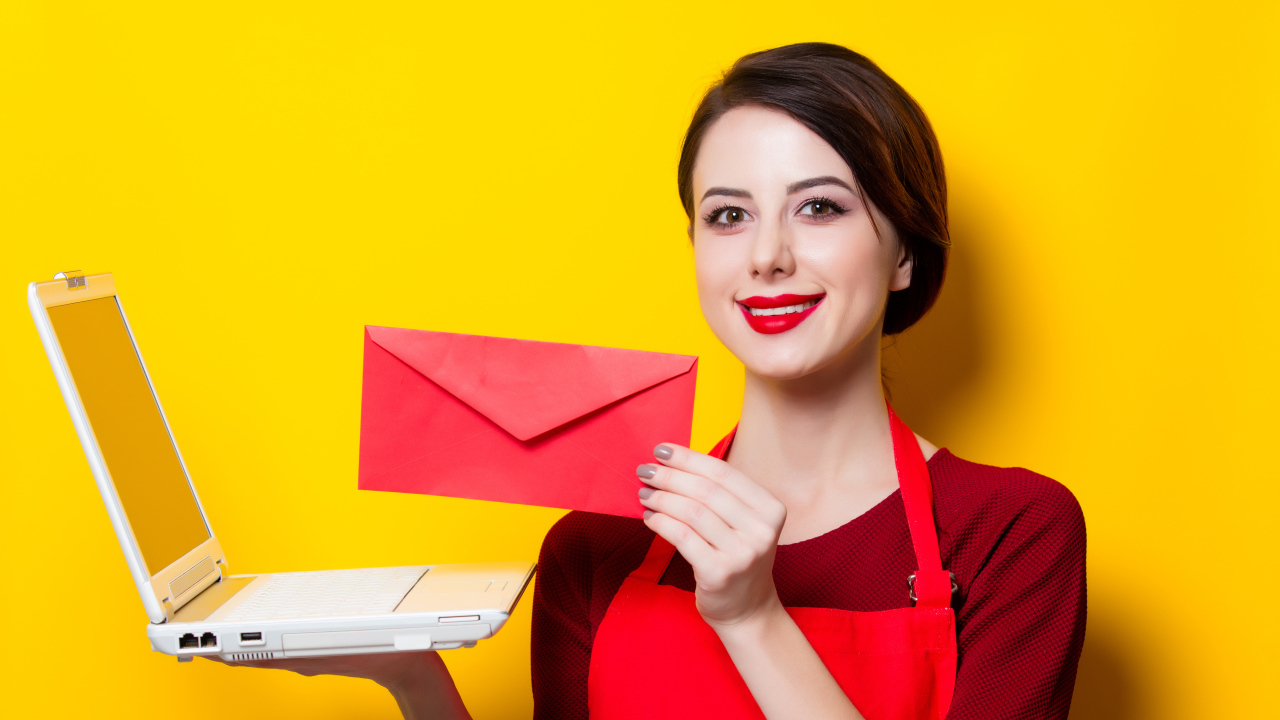 Улыбающаяся девушка с ноутбуком и конвертом в руках на желтом фоне