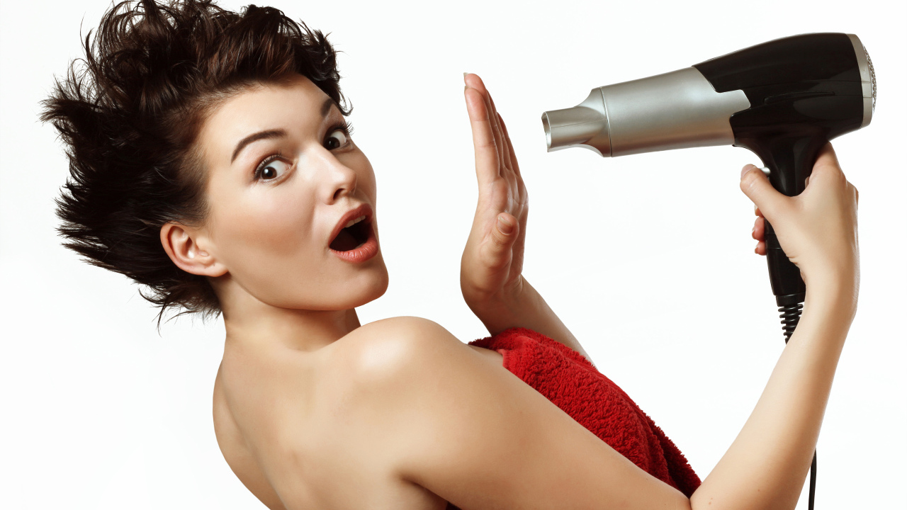 Удивленная девушка с феном в руках на белом фоне