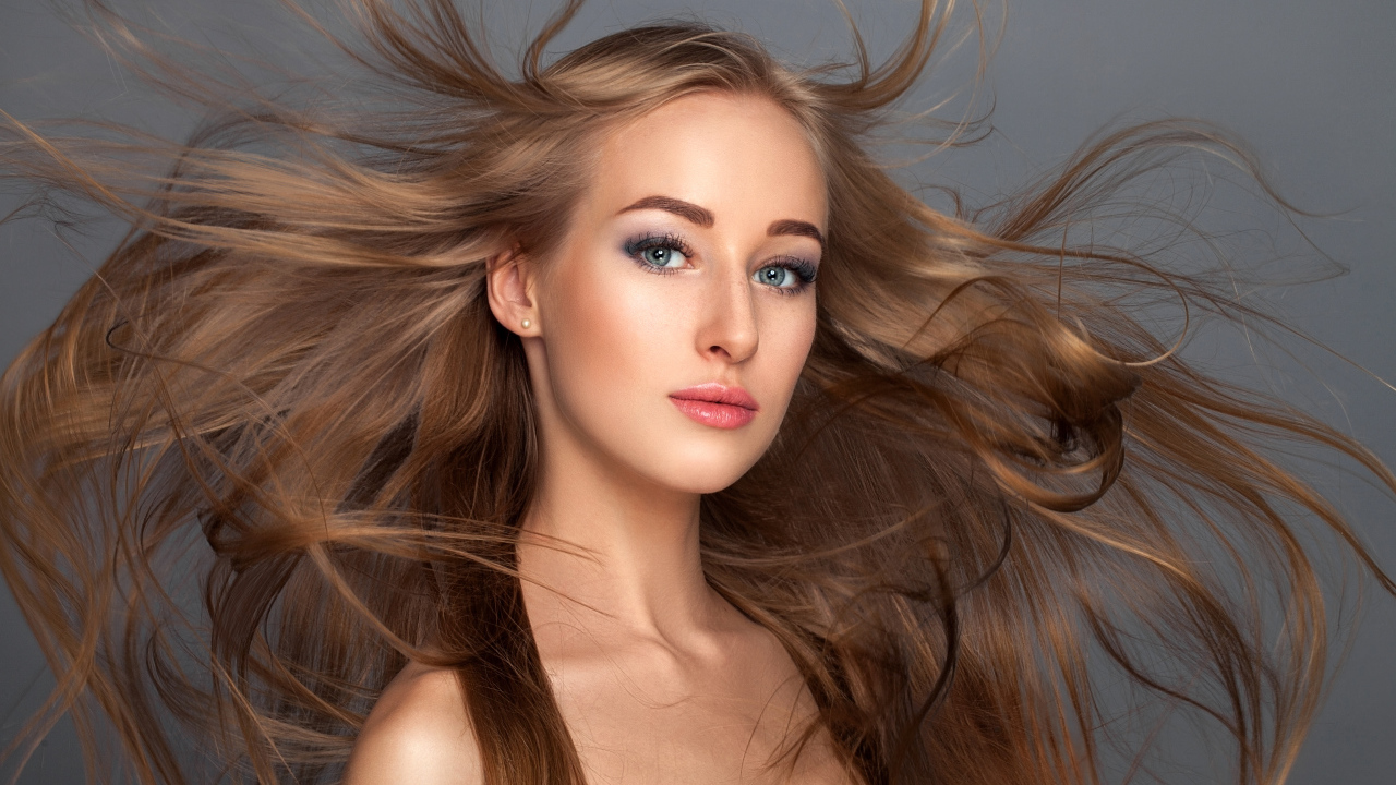 Ветер развивает волосы красивой девушке на сером фоне