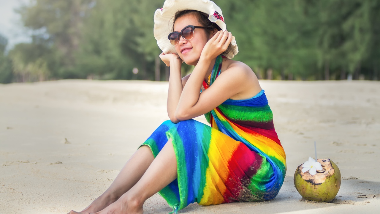 Молодая азиатка сидит на берегу с кокосом