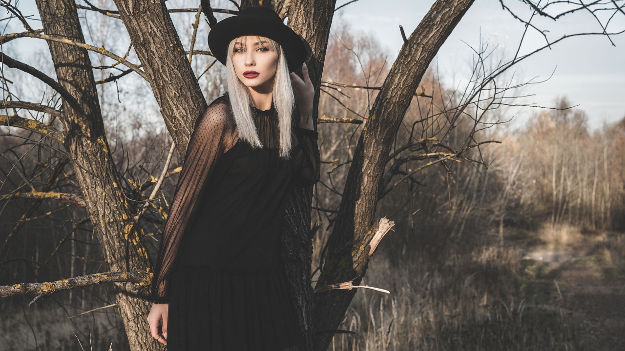 Молодая блондинка в черной шляпе у дерева