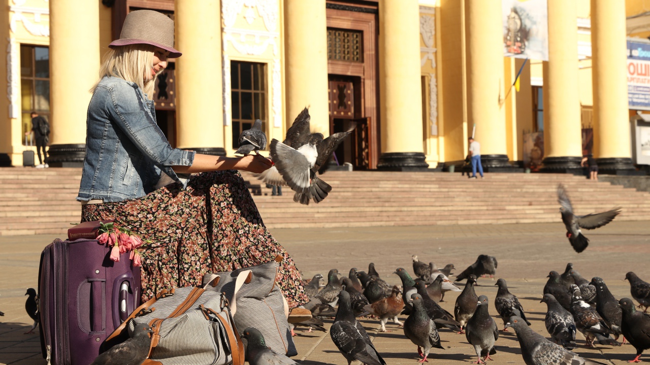 Молодая девушка кормит голубей на вокзале