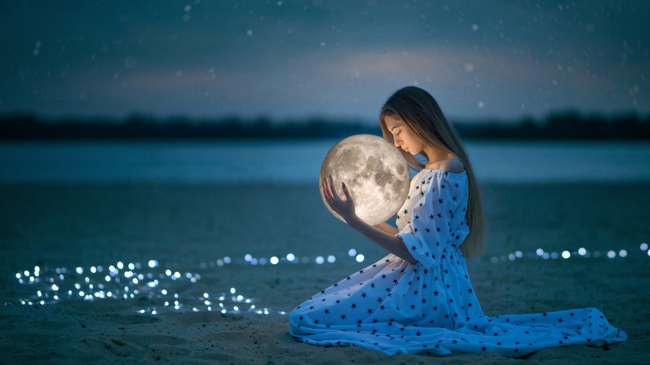 Молодая девушка в красивом платье с луной в руках на песке