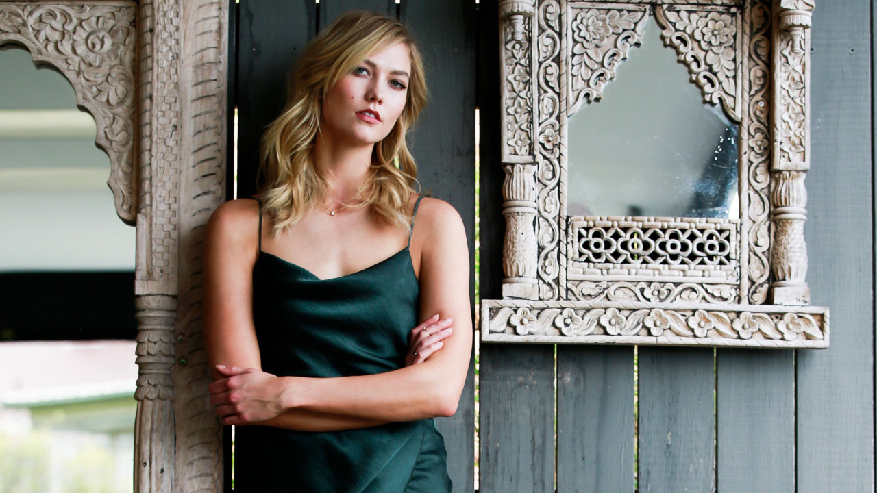 Красивая стильная модель Карли Клосс стоит у стены с зеркалом