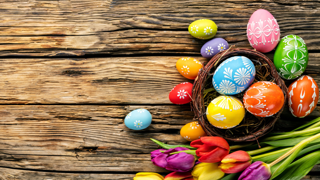 Крашеные пасхальные яйца с букетом тюльпанов на деревянном фоне