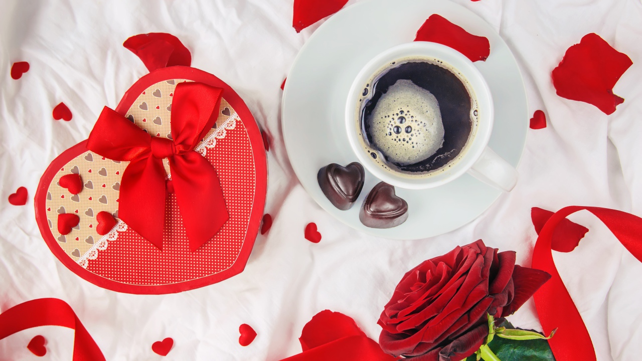 Кружка с кофе и шоколадными конфетами на столе с подарком и красной розой 