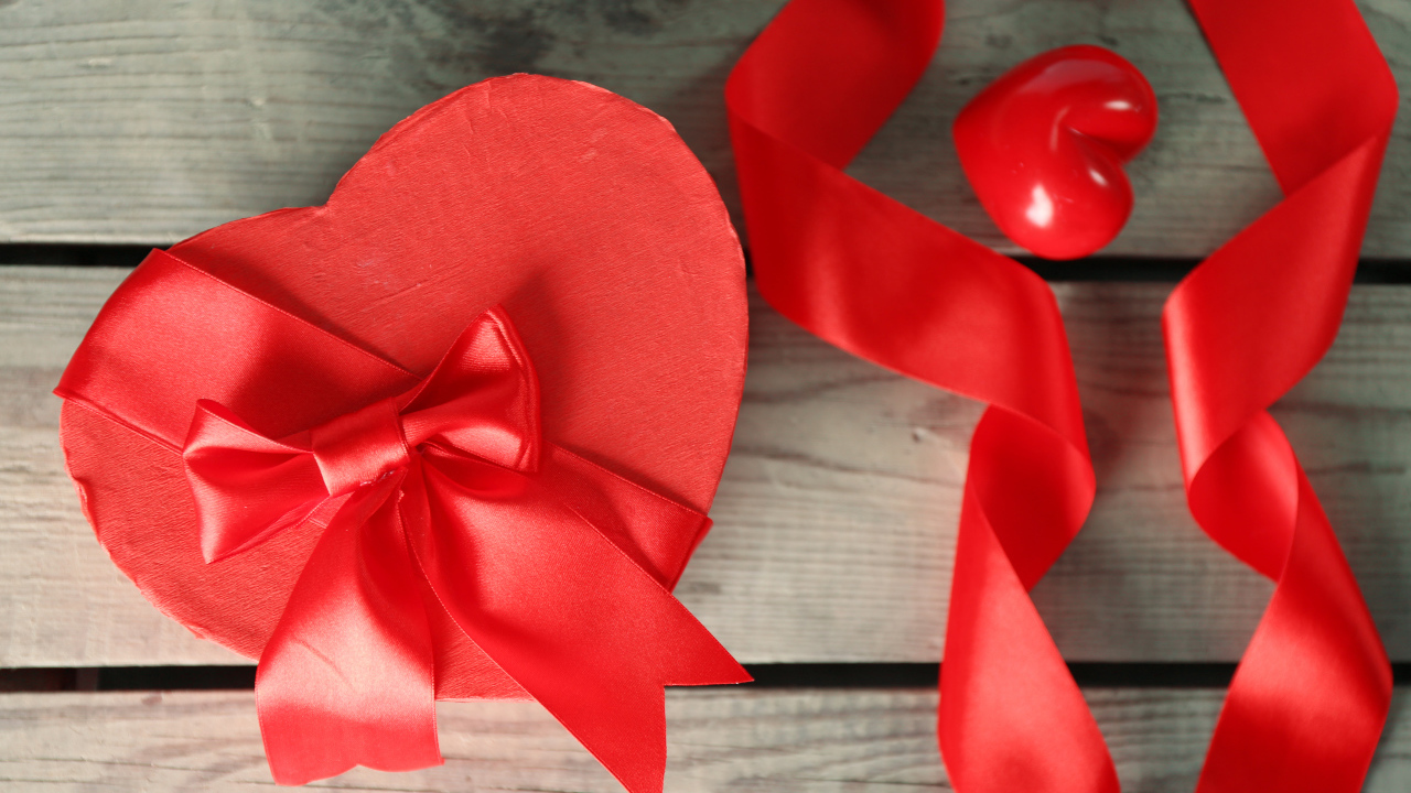 Красная коробка в форме сердца на деревянном столе с красными лентами