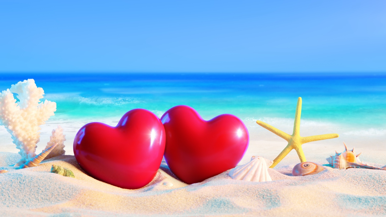 Два красных сердца на белом песке с ракушками на фоне моря