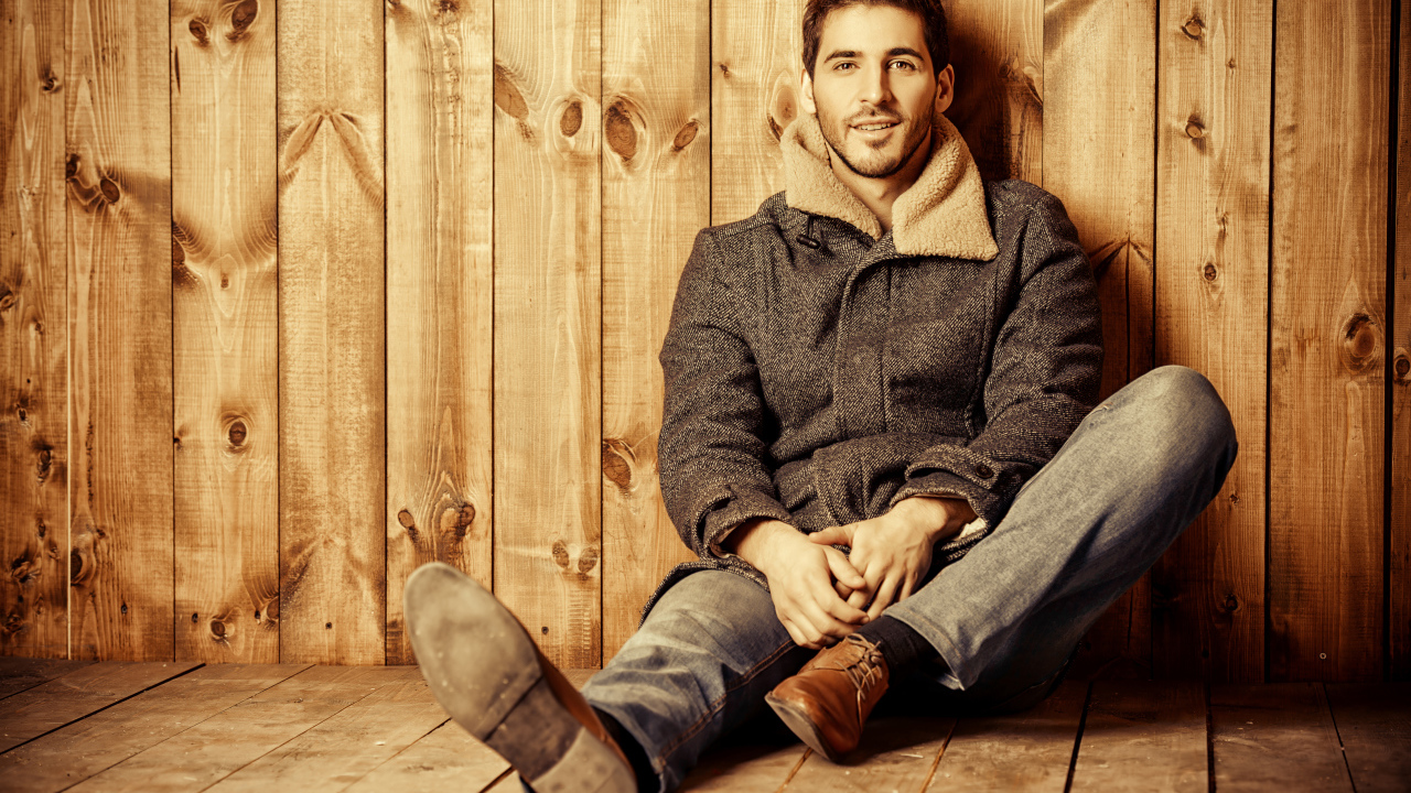 Молодой мужчина в пальто сидит у стены