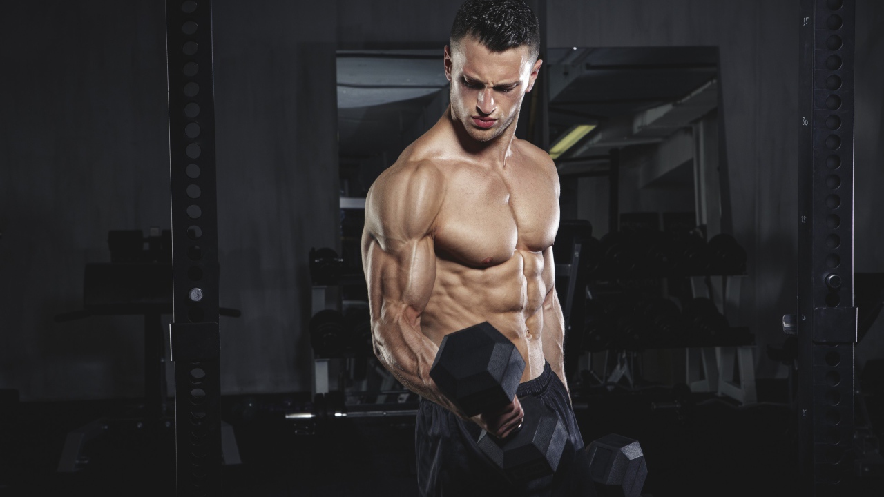 Накаченный мужчина с тяжелыми гантелями в руках 