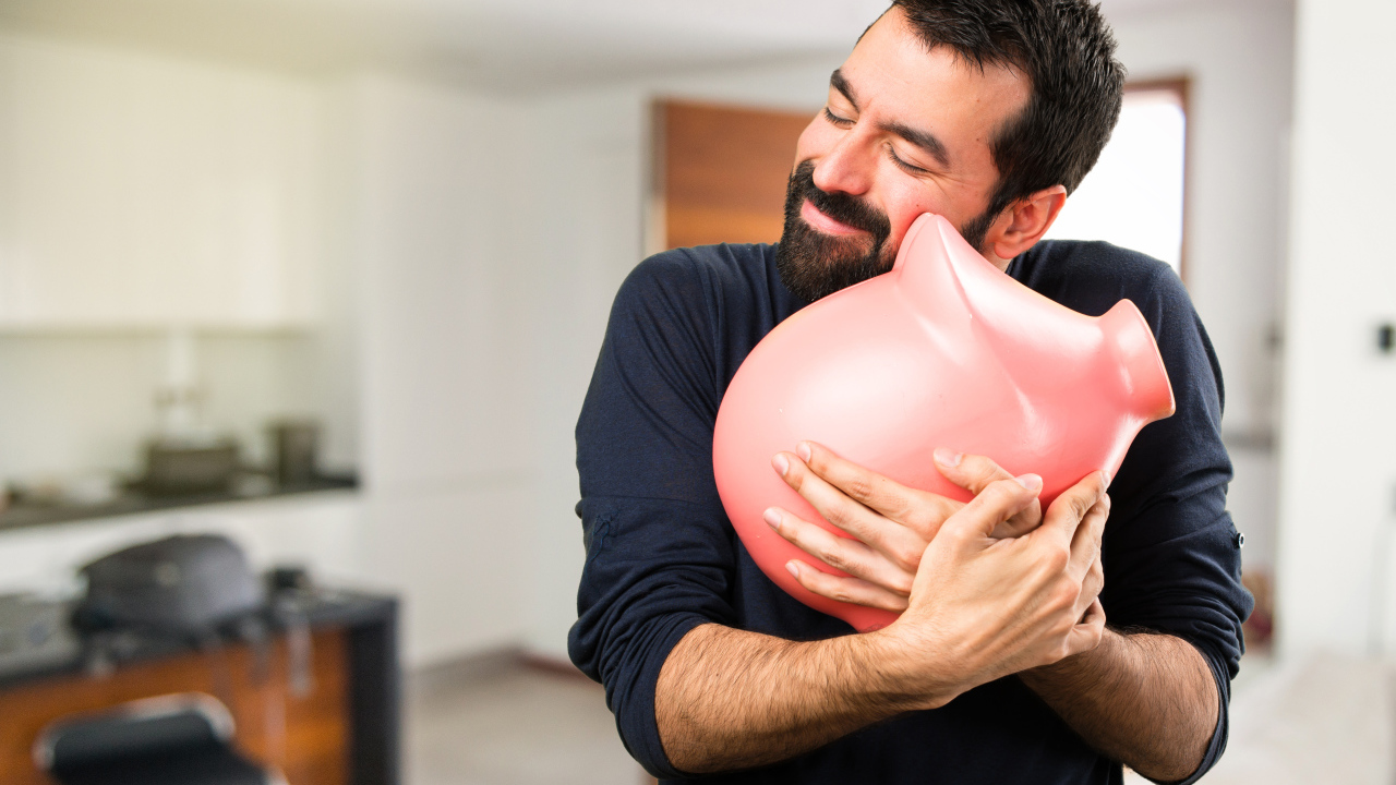 Мужчина обнимает розовую свинью копилку 