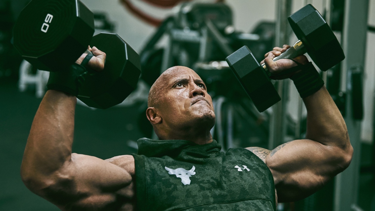 Американский актер, сильный мужчина Дуэйн Джонсон с гантелями в спортзале