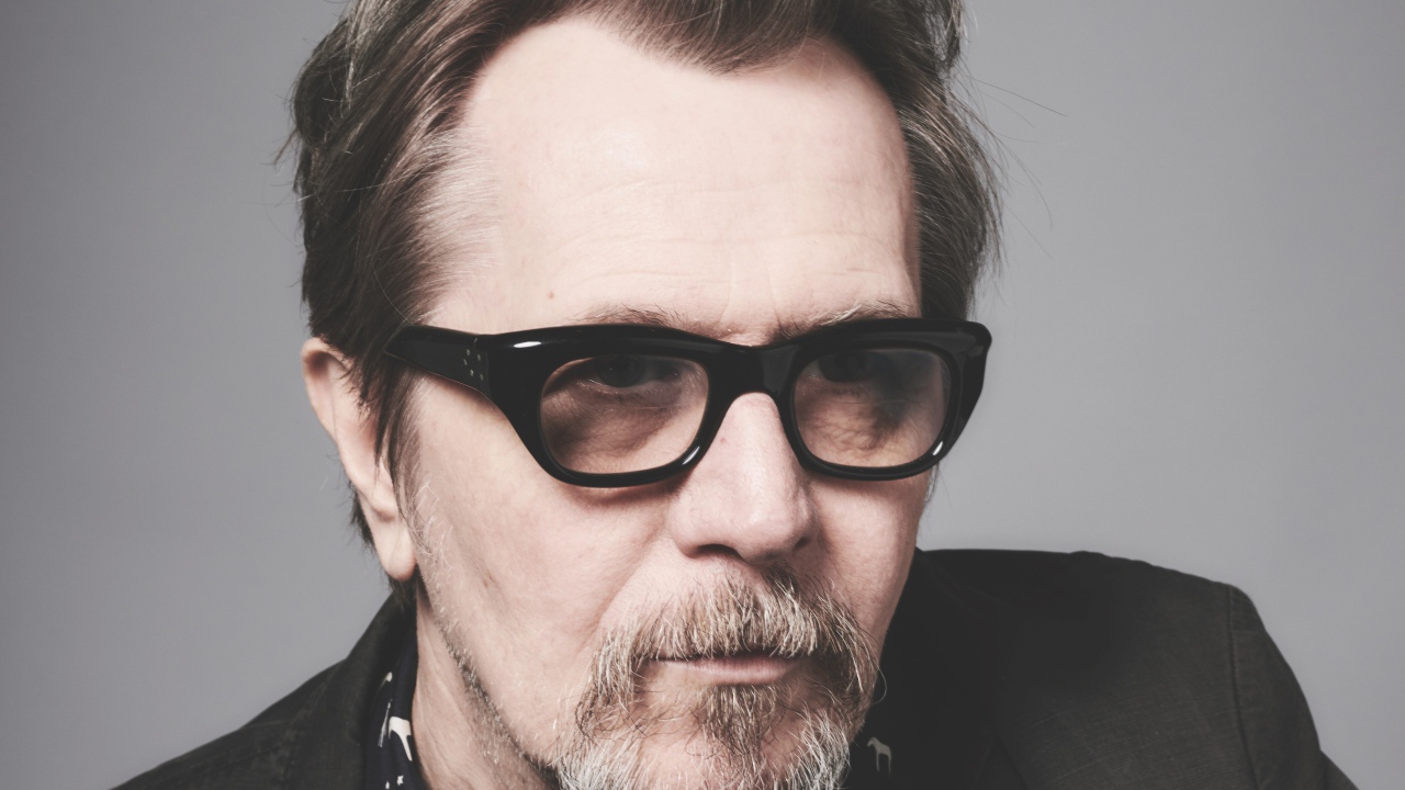 Английский актер Гэри Олдмен в очках на сером фоне