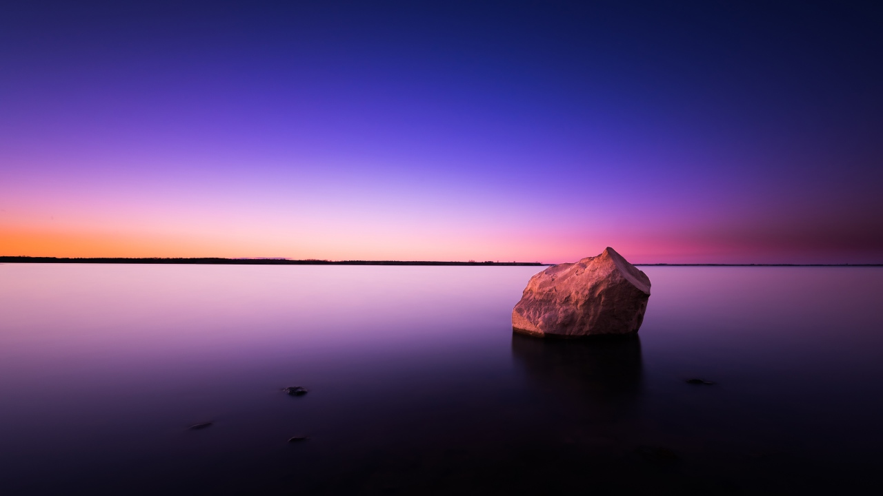 Big stone in calm water at dusk