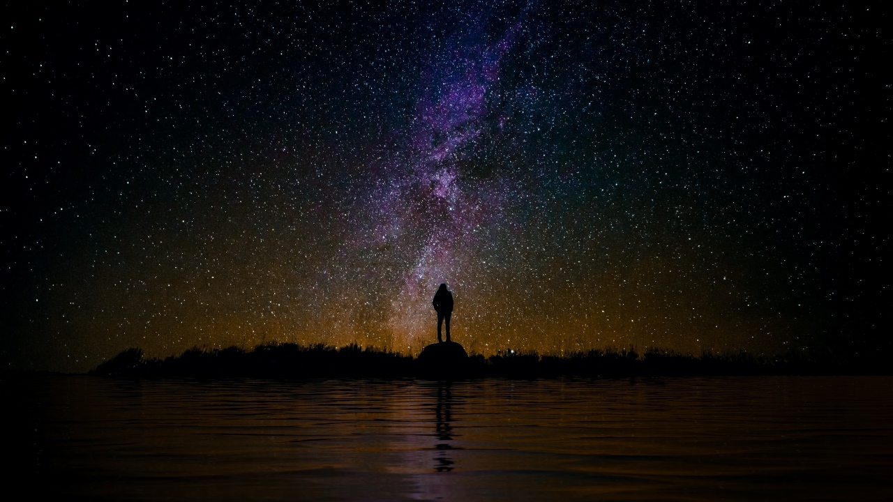 Силуэт человека стоит на камне у воды под звездным небом