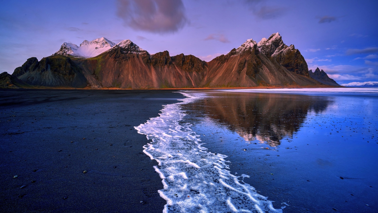 Вода на черном песке на фоне гор 