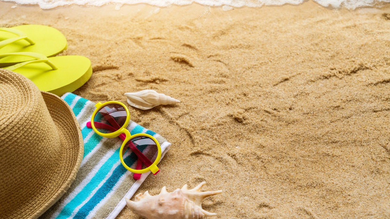 Шляпа, очки, полотенце и ракушки на желтом песке у моря