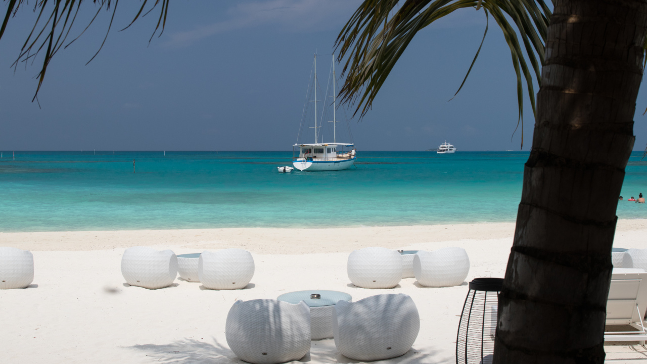 Белые кресла и столики на белом песке на пляже у голубой воды