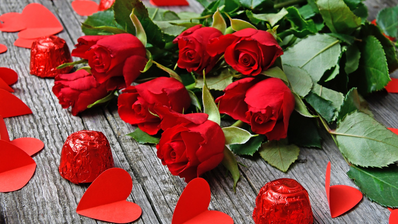 Букет красных роз на деревянном столе с конфетами и красными сердечками