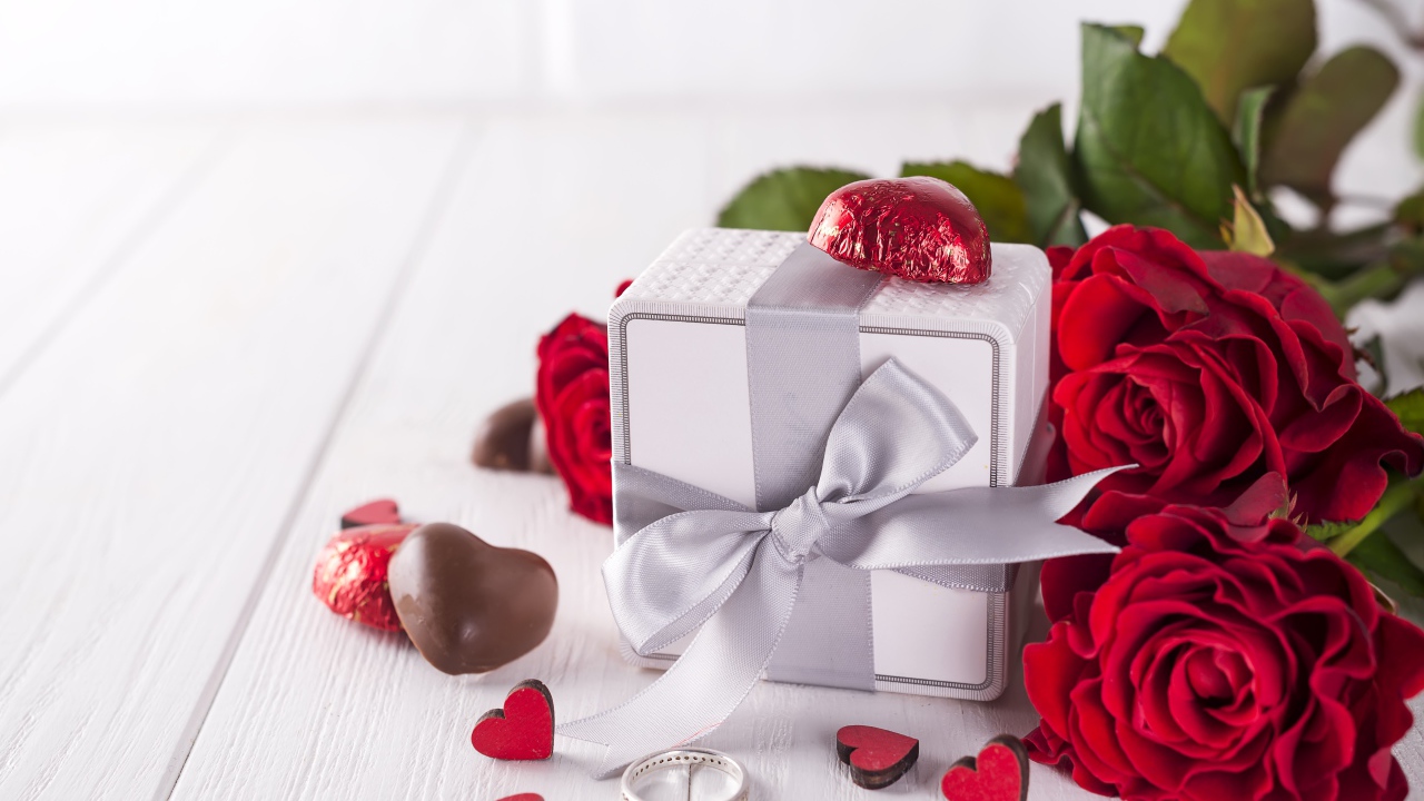 Подарок на столе с конфетами и букетом красных роз 