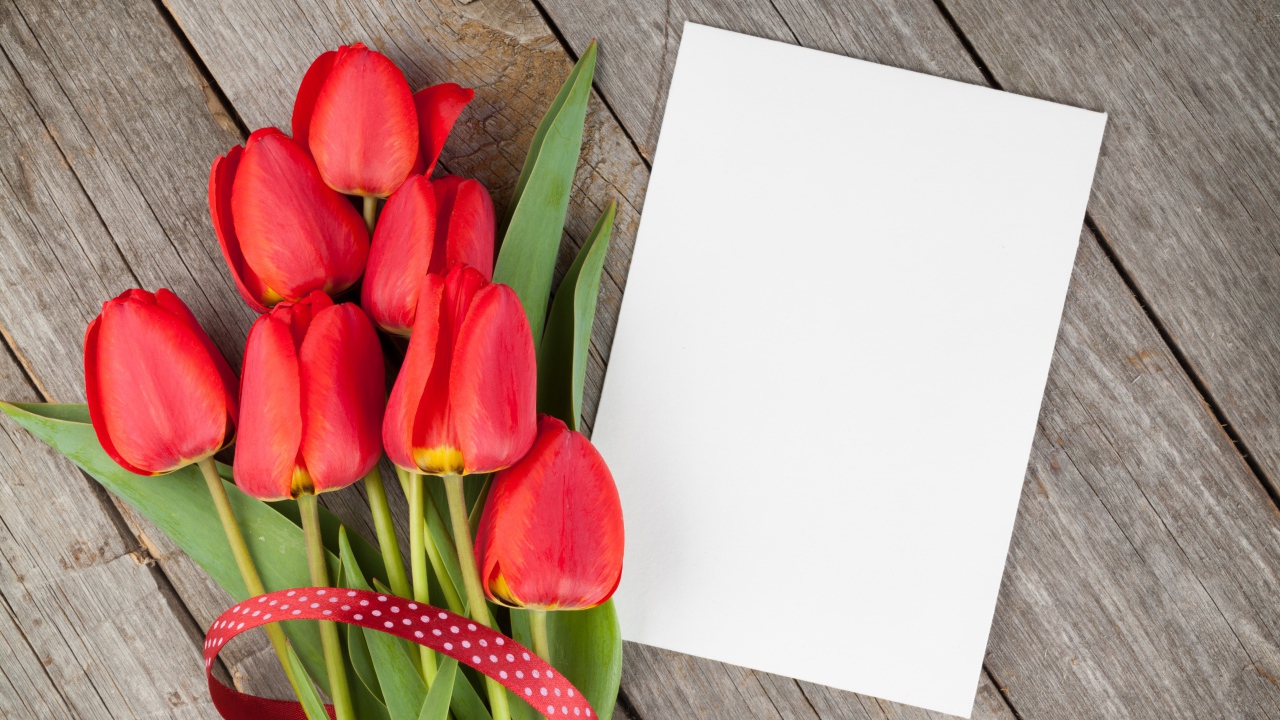 Букет красных тюльпанов с листом бумаги на деревянном столе