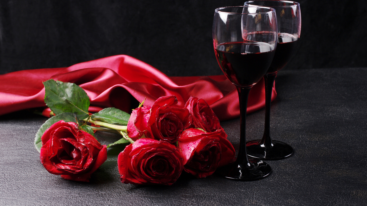 Два бокала с красным вином на черном фоне с букетом красных роз