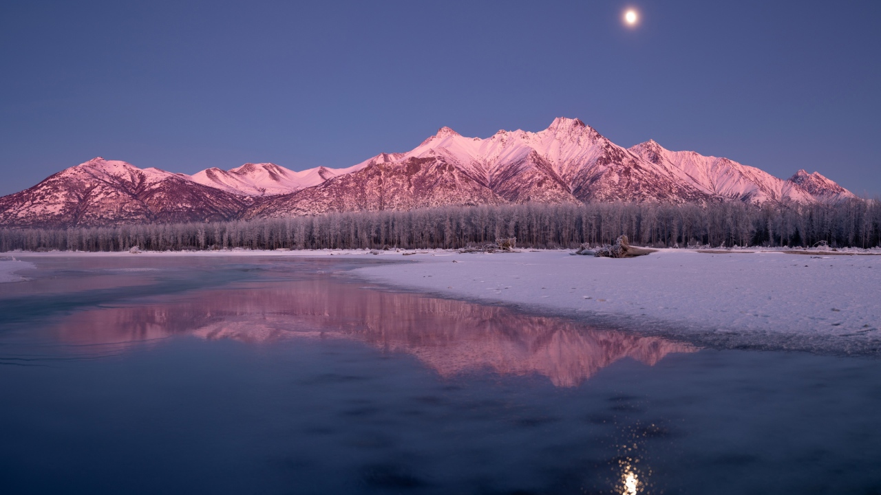Луна над заснеженными горами отражается в заледеневшем озере 