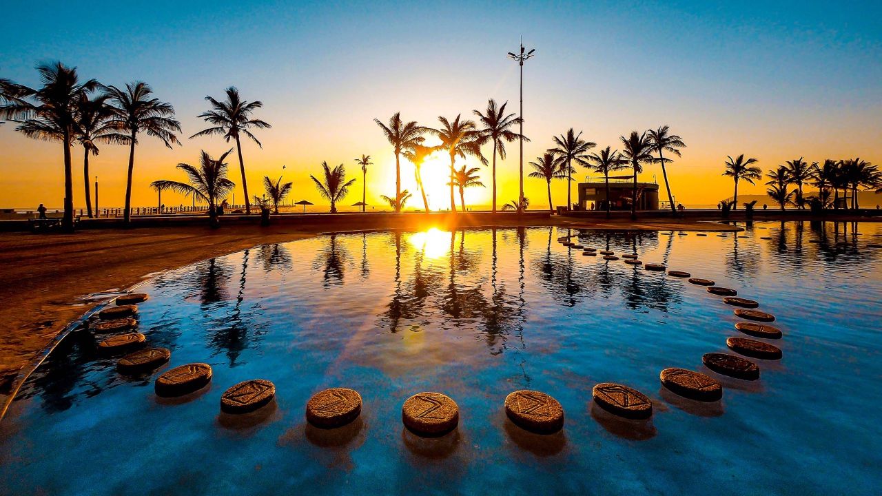 Закат солнца на тропическом пляже на фоне бассейна