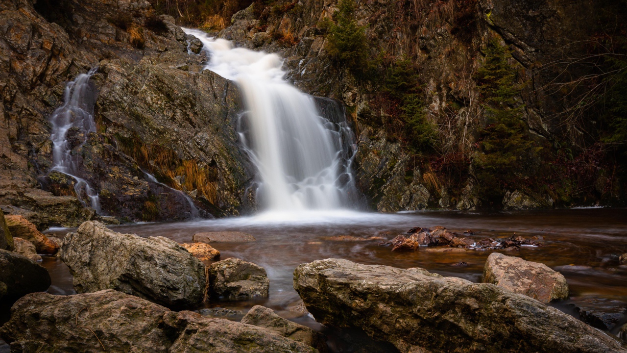 Быстрая вода водопада стекает по камням в горную реку