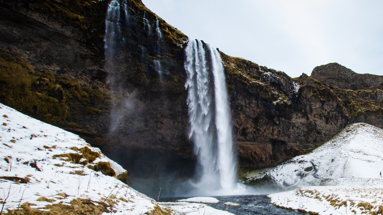 Водопад стекает со скалы в реку с покрытыми снегом берегами