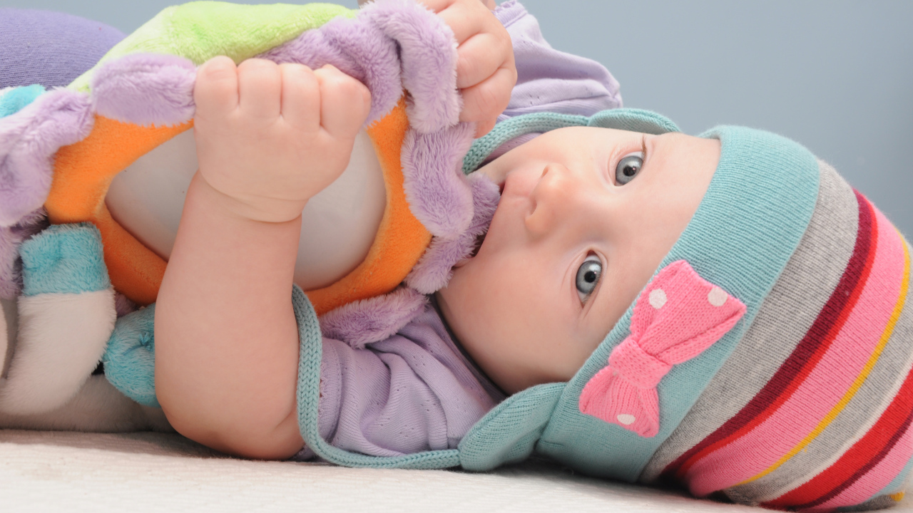 Младенец в шапке грызет мягкую игрушку