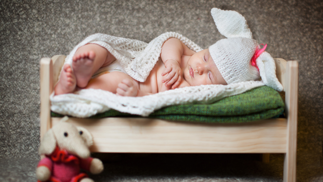 Маленький спящий ребенок в шапке с ушками спит на кровати