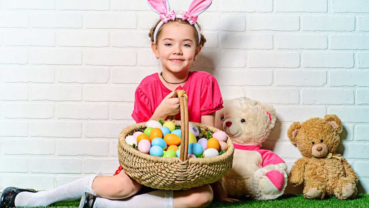 Улыбающаяся девочка сидит у стены с корзиной пасхальных яиц и игрушками
