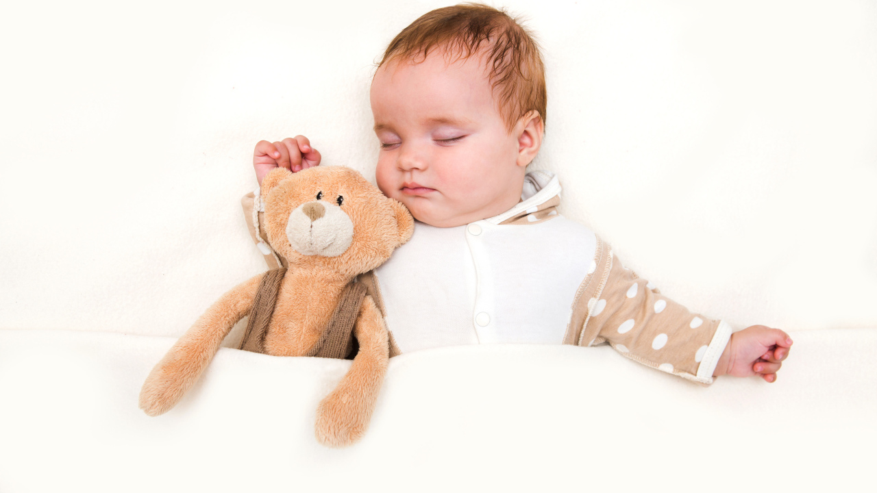 Грудной ребенок спит с плюшевым мишкой на белом фоне