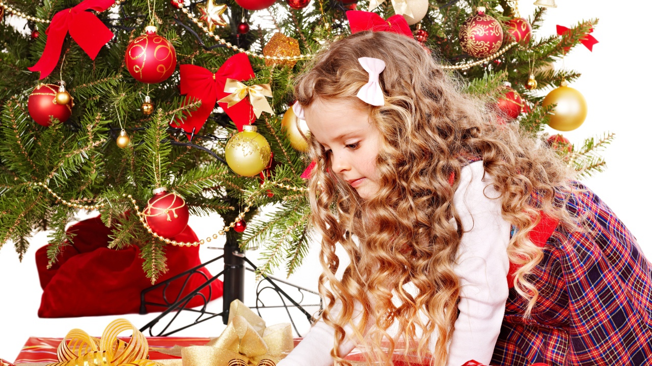 Красивая маленькая девочка смотрит подарки под елкой на новый год 