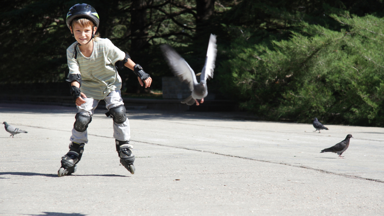 Мальчик катается на роликах на асфальте с голубями