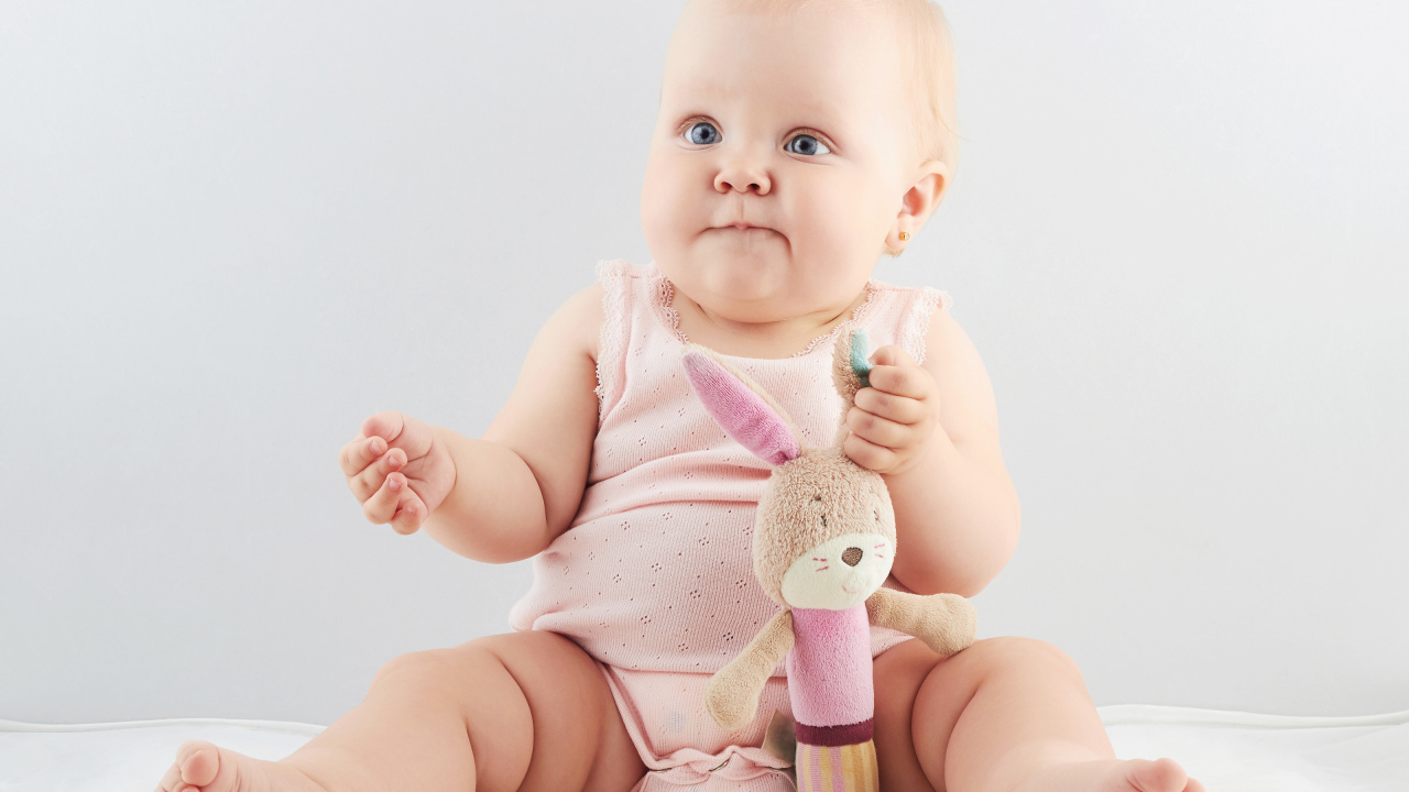 Смешной малыш с игрушкой сидит на сером фоне