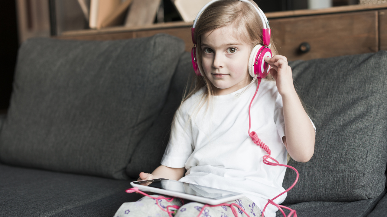 Девочка сидит на диване в наушниках  и с планшетом