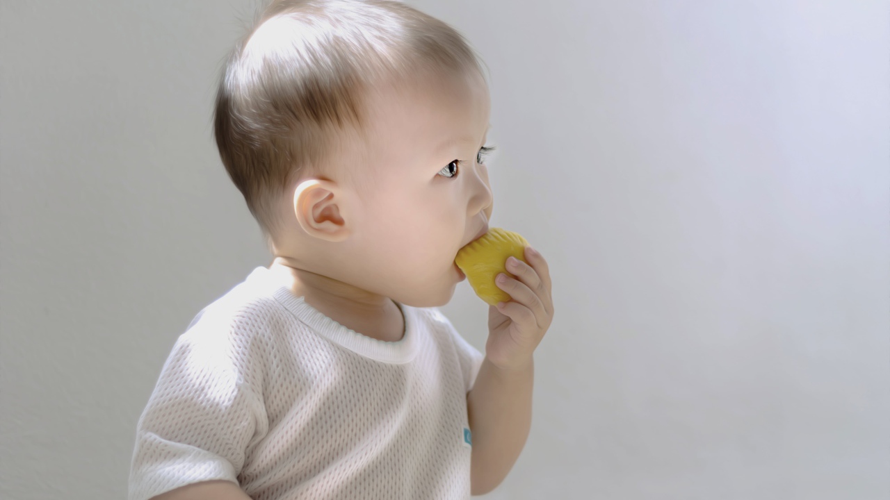 Маленький ребенок грызет игрушку на сером фоне