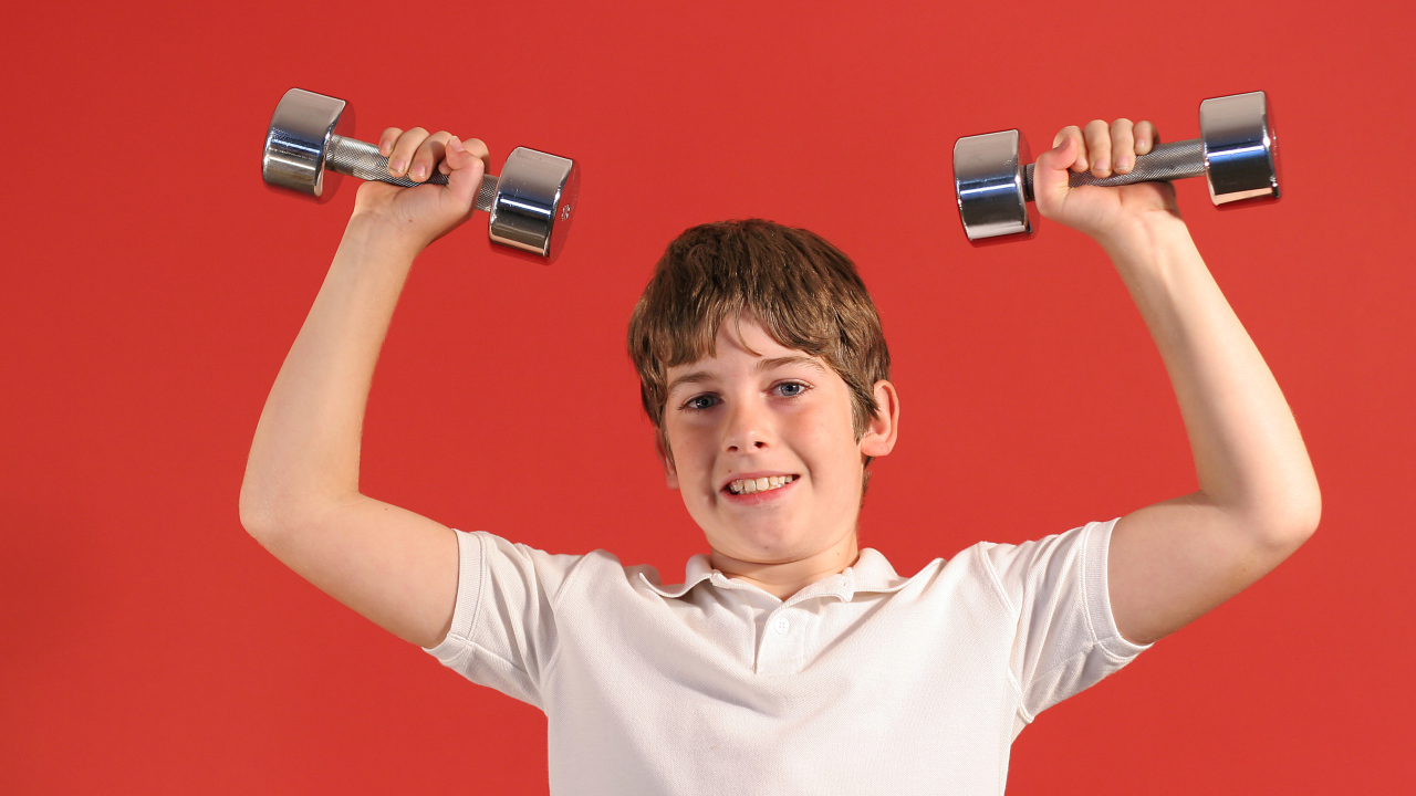 Маленький мальчик с гантелями на красном фоне